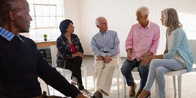 Senior man looking at friends talking while sitting on chair senior support group