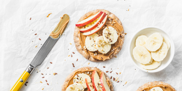 Peanut butter, apple, banana, flax and chia seed crackers toast on a light background, top view whole grain crackers