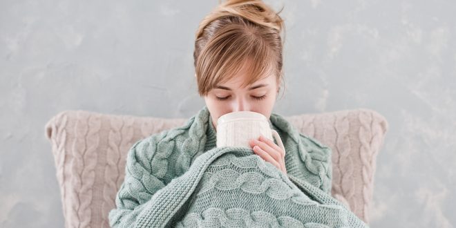 Attractive woman with cup of hot drink Attractive woman with natural blond hair posing without makeup with white cup of hot drink wrapped with blanket at home