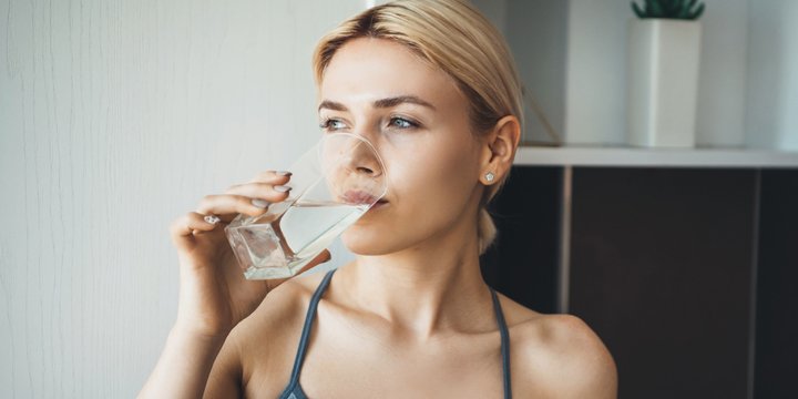 Young fitness lady drinking water after yoga exercises wearing sportswear at home in the kitchen