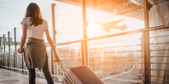 Young woman pulling suitcase in airport terminal. Copy space travelling