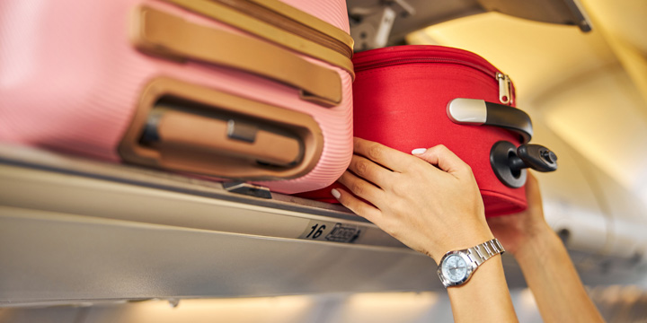 Hands laying down a carry-on baggage on an upper shelf travel bag