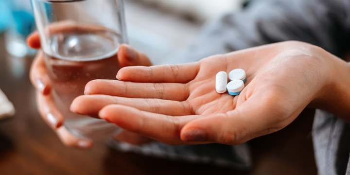 Businesswomen working at home with glass of water takes white round pill in hand.