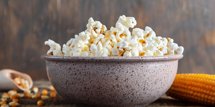 Freshly cooked popcorn in a bowl on a wooden table. Traditional American maize snack.