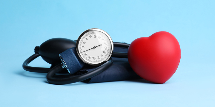 Blood pressure meter and toy heart on light blue background