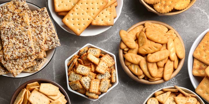 Different delicious crackers in bowls on grey table, flat lay