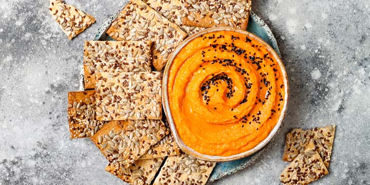 Pumpkin hummus seasoned with olive oil and black sesame seeds with whole grain crackers. Healthy vegetarian appetizer or snack