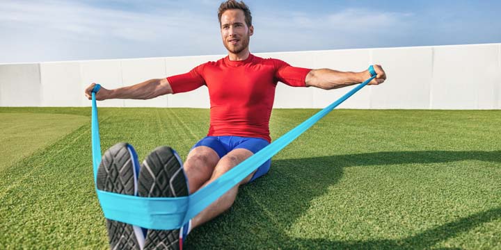 Resistance bands fitness man training with elastic band at outdoor gym park. Athlete doing dynamic workout pulling rubber elastics plyometrics exercises