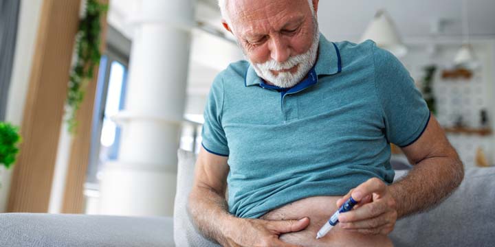 Senior man using lancet pen at home. Diabetes control Mature man sitting and injecting insulin insulin injection