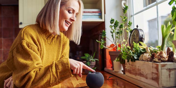 Happy mature woman using smart speaker at home in a kitchen digital assistance for seniors