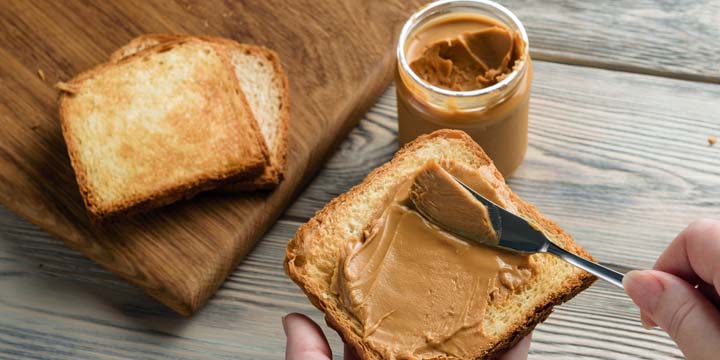 Female hands spread peanut butter on toast close-up.